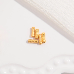Detailed view of five golden S925 silver cylinder beads with diamond grid texture on white cloth