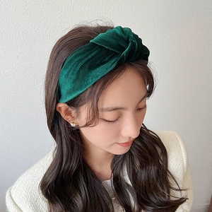 Detail of a wide dark green velvet knotted headband worn by a model in soft lighting