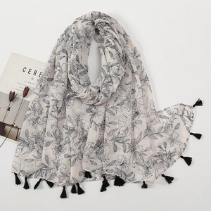 Detailed flat lay of beige scarf with black lily flower prints and fringe trim detail