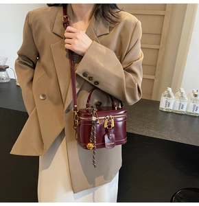 Detail of burgundy leather box bag with gold buckle hardware worn over khaki blazer