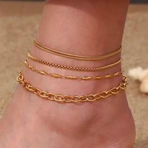 Detail of four gold-plated stainless steel anklets styled on a model at the beach