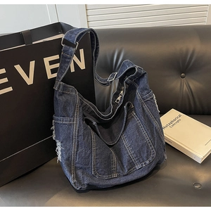 Détail du grand cabas en jean bleu foncé avec surpiqûres sur canapé en cuir noir