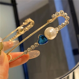Detailed close-up of golden safety pin brooch with a blue heart crystal and white pearls