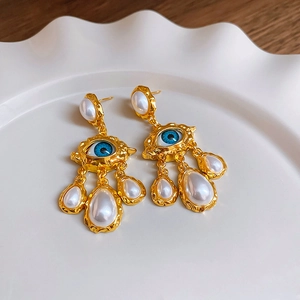 Close-up of vintage gold evil eye earrings with white drop pearls on a ceramic tray