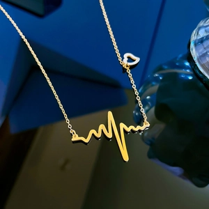 Close-up of golden heartbeat pulse line pendant and small hollow heart on a sleek chain