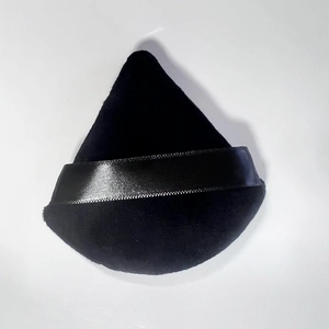 Detailed view of a soft black triangular powder puff with a satin ribbon handle on white backdrop