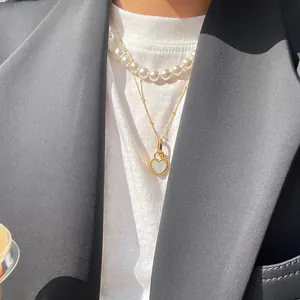 Detail of layered gold heart necklace with white pearls on a model wearing a blazer