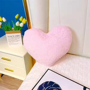 Coussin en peluche rose en forme de cœur avec texture douce sur un lit blanc chic