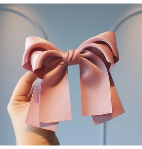 Detailed close-up of a pink satin multi-layer bow hair clip with smooth silk texture