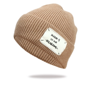 Detailed knit texture of a caramel beanie with a white SEASONS 13 textile patch