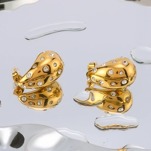 Elegant gold teardrop hollow earrings with inlaid crystals on a reflective water surface