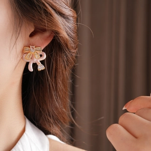 Detail of elegant bow earrings with pink enamel heart pendant on a model ear