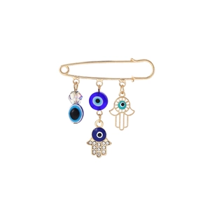 Detailed close-up of golden tassel brooch with blue evil eye and Hamsa Hand charms