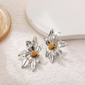 Close-up of flower earrings with silver petals and gold center on textured background