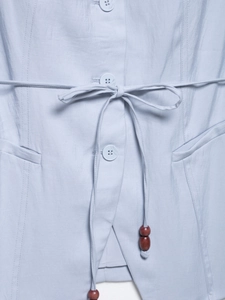 Detail of light blue vest featuring resin buttons, waist drawstring and dark wood beads