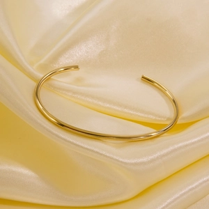 Detail of a minimalist gold-plated open bangle on elegant yellow silk fabric