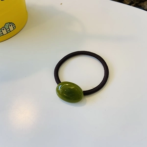 Macro shot of polished dark green oval bead on a durable black elastic hair tie