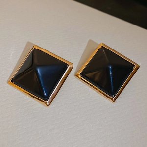 Détail des boucles d'oreilles carrées en résine avec bordure dorée et centre pyramide noir