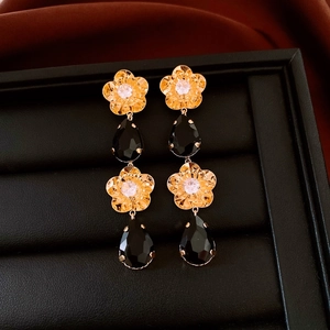 Détail de boucles d'oreilles fleur plaquées or 18 carats avec gouttes noires et boîte luxe