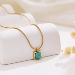 Gros plan d'un collier chaîne serpent dorée avec un pendentif carré en turquoise