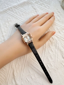 Close-up of a women's vintage square gold watch with black leather strap on a wrist