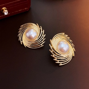 Macro shot of vintage irregular gold spiral earrings with elegant pearls on leather surface