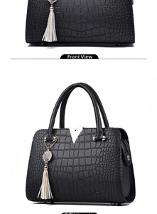 Close-up of black crocodile pattern handbag with gold V-buckle and light tassel detail