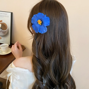 Blue hibiscus flower hair clip styled on model's brown hair in a cozy cafe setting