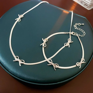 Detailed macro view of silver bow-knot snake chain necklace and bracelet on jewelry mat