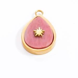 Macro detail of a teardrop-shaped gold pendant with pink stone and star emblem