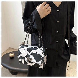 Detalle del bolso bandolera con estampado de vaca, cadena negra y cierre metálico