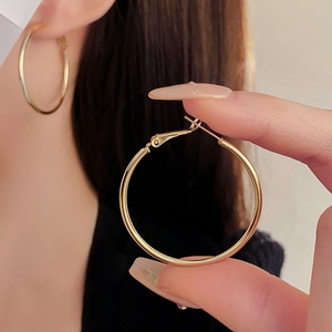 Close-up of elegant gold metal hoop earrings held in hand with model background