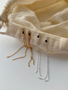 Detail of silver and gold tassel earrings with black stones hanging on a fabric pouch