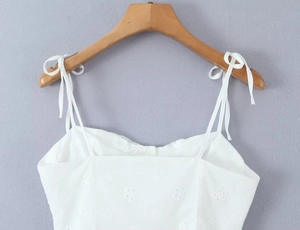 Detail of white camisole top with floral embroidery, thin straps and bow decoration