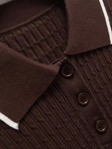 Detail eines schokobraunen Strickpolos mit weißem Kontrastrand und Rippenstruktur