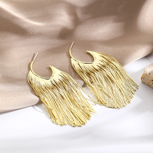 Detail of elegant gold tassel earrings featuring long chains on soft champagne silk fabric