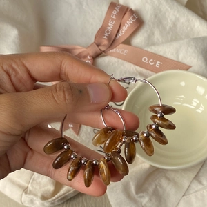 Detail of silver hoop earrings with amber resin teardrop charms held in hand