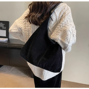 Close-up of a large black suede hobo bag styled on a model wearing a white sweater