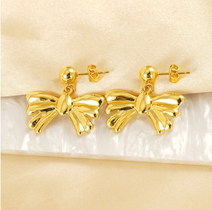 Macro shot of polished gold bow stud earrings on marble and champagne silk surface