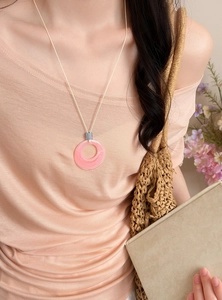 Close-up of a pink marbled circular pendant necklace paired with a soft peach summer outfit