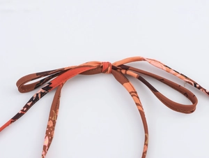 Detail of a brown and orange abstract print tie-knot bow on vacation style clothing