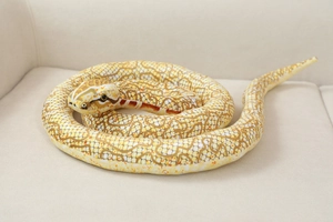 Detailed close-up of realistic plush snake toy with brown mesh texture on a beige sofa