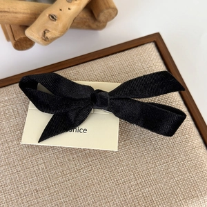 Detailed close-up of a black velvet bow hair clip with textured fabric on a display card