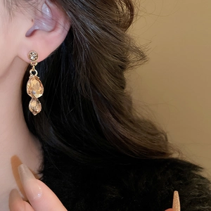 Detail of elegant gold drop earrings with champagne crystals on a model's ear