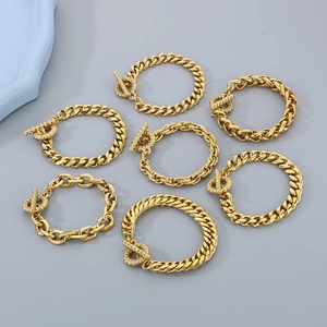 Set of seven gold-colored stainless steel Cuban link bracelets with T-bar clasps on grey