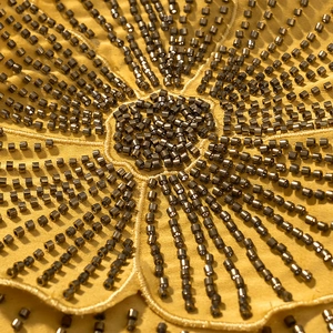 Close-up of intricate flower beadwork and metallic sequins on yellow halter dress fabric