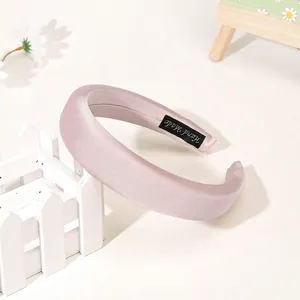 Detail of light pink satin headband featuring a black 'Hand Made' woven inner label