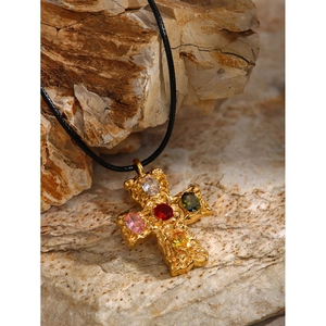 Macro detail of a vintage 18k gold cross pendant with multi-colored embedded gems