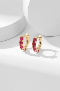Macro detail of gold huggie earrings featuring vibrant micro-pave red cubic zirconia