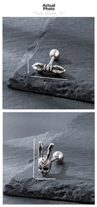 Macro detail of retro steel rabbit skull and vajra stud earrings on black stone